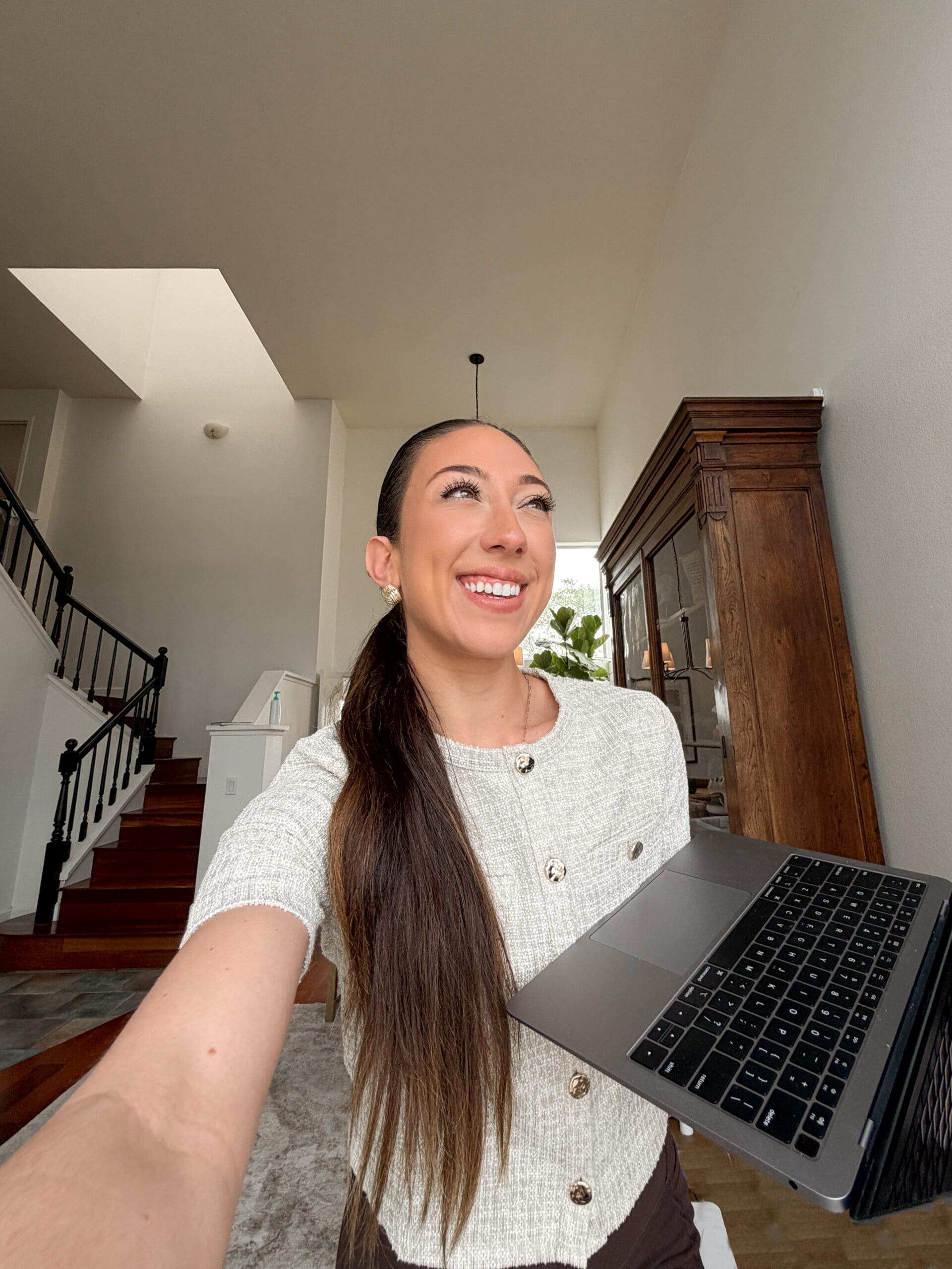 Millie taking a selfie with one hand and holding her laptop with the other.